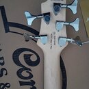 Záběr na hlavu světlé dřevěné basové kytary s chromovanými ladicími kolíky. Na zadní straně jsou nápisy Action Bass V Plus, S/N: IE251104182 a značen…