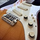 Elektrická kytara s barevným přechodem těla od červené přes žlutou po hnědou a bílým pickguardem. Na krytkách tří snímačů je uveden nápis Fender. Kyt…