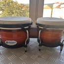 Dvojice bongoů s hnědým lesklým povrchem korpusů a bílými membránami. Na levém korpusu je bílý oválný štítek s nápisem Lp Matador Custom. Nástroj má…
