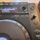 Detailní pohled na ovládací panel černého DJ decku. Na displeji jsou vidět nápisy TRACK01, TRACK02 a TRACK03, pod ním je text MP3/AAC/WAV/AIFF. Panel…