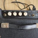 Horní ovládací panel černého basového komba s texturou kůže. Na panelu jsou bílé ovratové knofíky a nápisy INPUT, VOLUME, BASS, MID, TREBLE, AUX IN,…