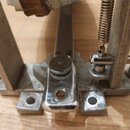 Detailní pohled na kový mechanismus pedálu v stříbrné barvě. Součástí jsou pružina, nastavitelné šrouby a kovová základna s otvory pro připevnění. Po…