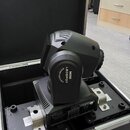 Černý LED reflektor typu moving head umístěný v transportním kufru s hliníkovými hranami. Na přístroji je bílý nápis MINI LEDSPOT MOVING HEAD LIGHT a…