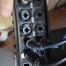 Detailní pohled na zadní panel černého elektronického zařízení s několika konektory. Jsou zde vidět zapojené kabely v portech označených nápisy "Inpu…