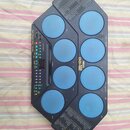 Elektronický bicí pad modré barvy s černým plastovým rámem. Na přístroji je nápis YAMAHA a model DD-12, dále text Super Session Pad / Player / Scrape…
