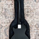 Černá elektrická kytara s dvojcutem, položená na černém polstrováním (gig bag). Na hlavě je nápis PROVIDENCE. Zadní strana krku a těla je v matně čer…