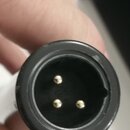 Detailní pohled na konektor s třemi zlatými piny v černém plastovém těle. Povrch černého plastu vykazuje drobné škrábance a opotřebení. Žádné značky…