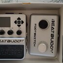 V bílém kartónovém boxu jsou dvě stříbrná zařízení. Levý pedál má nápisy BEATBUDDY a Singular Sound, horní ovládací panel s displejem a popisky Volum…
