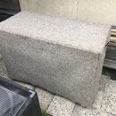 Šedý obdélníkový reproduktorový box potažený hrubým kobercovým materiálem. Na viditelných stranách nejsou žádné značky, loga ani nápisy. Povrch vykaz…