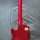 Zadní strana červené elektrické kytary s tvarem Les Paul. Na těle je zlatý oválný štítek s nápisy Gibson, 1957-1960 a MADE IN USA. V dolní části těla…