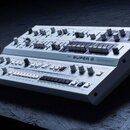 Bílý analogový syntetizátor s výrazným nápisem UDG SUPER 6. Přístroj má rozsáhlý ovládací panel s mnoha posuvníky, otočnými knoflíky a bílými tlačítk…