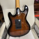 Zadní strana elektrické kytary s tmavě hnědým sunburst povrchem a světle dřevěným hnedým krkem. Na horní části těla je kovovádeska s nápisem "Made in…