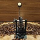 Černý basový pedál s kovovou konstrukcí a bílým, kulatým stupňem. Mechanismus obsahuje řetězový pohon a viditelnou pružinu s nastavovacími šrouby. Na…