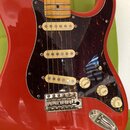 Červená elektrická kytara typu Stratocaster s hnědým želvovinovým pickguardem a javorovým hmatníkem. Na kytare jsou tři bílé snímače, chromovaný koby…