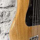 Detail korpusu basové kytary z přírodního dřeva s viditnou masivní strukturou. Nástroj má černý pickguard a chromovaný most s четыřmi strunami. Na hr…