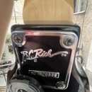 Detail zadní strany hlavy kytary z přírodního dřeva s chromovaným krytem ladicí mechanismy. Na černém plastovém panelu je bílý nápis B C Rich TM a ní…