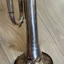 Detailní pohled na spodní část mosazného nástroje stříbrnou barvou. Na trubici je vyryto logo s nápisy AMATI a pod ním kurzívou K. Gussloff. Spodní č…
