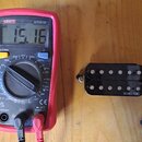 Na fotografii je červený digitální multimetr značky UNI-T, model UT131B, který na displeji zobrazuje hodnotu 15.16. Vedle něj leží černý humbucker s…