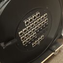 Černý kabelový navíjač s panelem konektorů. Na panelu jsou nápisy MAIN L, MAIN R, AUX 1, AUX 2, AUX 3, AUX 4, AUX 5 a AUX 6 a číslování od 1 do 32. V…