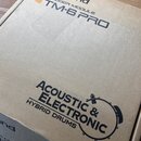 Kartonová krabice s nápisy. V horní části je logo Roland a text TRIGGER MODULE TM-6 PRO. Ve spodní části je nápis ACOUSTIC & ELECTRONIC HYBRID DRUMS…