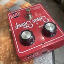 Červený efekt pedál s bílým nápisem Sonic Stomp a logem BBE. Na horní straně jsou dva černé oválné knoflíky a jeden kovový spínací tlačítko. V horní…