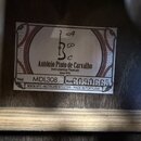 Detailní záběr na bílý papírový štítek s logem a textem, který je nalepen uvnitř hudebního nástroje. Štítek obsahuje nápis „António Pinto de Carvalho…