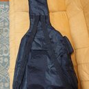 Černý textilní obal na hudební nástroj s ramenními popruhy. V horní části je bílý nápis ROCKBAG a pod ním menší text by Thomann. Povrch materiálu vyk…