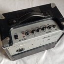 Černý kytarový kombo zesilovač s koženým potahem a kovovými rohy. Na horním ovládacím panelu jsou nápisy POWER, PHONES, BASS, MID, TREBLE, VOLUME, GA…