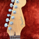 Hlava elektrické kytary z přírodního světlého dřeva s šesti stříbrnými ladičkami. Na povrchu je černý nápis Fender® STRATOCASTER MADE IN U.S.A. Povrc…
