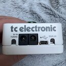 Bílý efekt pedál s nápisem tc electronic. Na horní straně jsou konektory označené texty 9V IN, TUNING a DISPLAY, přičemž u posledního je symbol USB.…