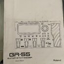 Fotografie znázorňuje bílou obálku uživatelské příručky. Uprostřed je černobílý nákres ovládacího panelu s nápisy Roland GR-55 GUITAR SYNTHESIZER, CO…