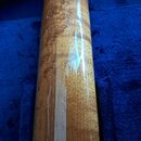 Detailní pohled na hmat krku nástroje vyrobený z lakovaného dřeva s výraznou masivní strukturou. Povrch je lesklý a vykazuje odrazy světla. Nástroj l…