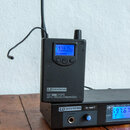 Černý bezdrátový přijímač a vysílač značky LD SYSTEMS. Na stojícím zařízení je nápis ME100G2BPR UHF PLL WIRELESS STEREO RECEIVER a modrý displej s ho…
