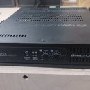 Černý rackový zesilovač s nápisem LUCIA 240/2M a logem LAB.GRUPPEN. Na předním panelu jsou dva ovratové ovladače s označením -10dB a -INF, kontrolky…