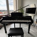 Černý digitální piano v podobě přímého pianina s lesklým povrchem a otevřeným víkem. Nad klávesnicí je vlevo nápis CASIO a vpravo modelové označení A…