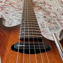 Detail elektrické kytary s hnědým dřevěným povrchem a tmavým hmatníkem. Na černé snímači je bílý nápis DiMarzio. Instrument vykazuje známky běžného p…