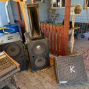 Na fotografii jsou tři černé reproduktorové bedny a míchací pult na stole. Pravá bedna nese v horní části písmeno K a v dolní části nápis YAMAHA. Stř…