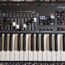 Klávesový nástroj s nápisem Legend One 61 KEYS STAGE KEYBOARD. Přístroj má stříbrný přední panel s mnoha ovládacími prvky, tlačítky a displejem, na k…
