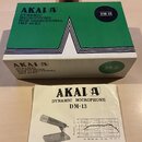 Zelená krabice a doprovodný manuál k dynamickému mikrofonu. Na obou předmětech je uveden název značky AKAI a model DM-13, dále nápisy DYNAMIC MICROPH…