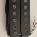 Dva černí elektrické snímače typu humbucker s viditelnými polosnovými póly. Povrch je černý, matný a vykazuje drobné škrábance a prach. Z pravého sní…