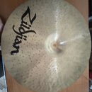 Zlatavý cymbál s viditelným kovánívým rýhováním po celém povrchu. Na levé straně je umístěno černé logo Zildjian. Povrch vykazuje drobné známky použí…
