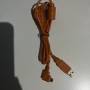 Oranžový USB kabel svázaný černou stahovací páskou. Na jednom konci je standardní USB-A konektor a na druhém konec typu micro-USB. Povrch kabelu i ko…