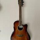 Akustická kytara s cutawayem v tmavě hnědém sunburst provedení. Na hmatníku a hlavě není vidět žádný nápis, ale na ozvukové desce je v rámci rozetové…