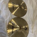 Dva mosazné činely typu hi-hat položené na bílém textilu. Oba mají černý nápis Zildjian a logo A s dopisem MASTERSOUND HIHAT. Spodní činel je mírně v…