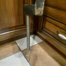 Detailní záběr na spodní část kovového stojanu nebo mechanismu. Povrch je v šedé barvě s viditelnými známkami opotřebení, odřeninami a Oxidací materi…