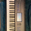 Černý digitální klavír s klávesnicí. Na horním okraji a na displeji je bílý nápis KORG, v pravém dolním rohu je nápis NAUTILUS MUSIC WORKSTATION. Nás…