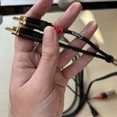 Ruka drží dva černé kabely s pozlacenými konektory typu jack. Na jednom z kabelů je viditelný bílý nápis CORDIAL a červený značovací kroužek. Kabely…