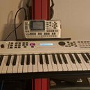 Bílá klávesová syntezátor s nápisy YAMAHA a MX61W. Nástroj má v horní části ovládací prvky, posuvníky a displej. V pozadí za syntezizátorem je umístě…