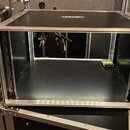 Černý transportní case s hliníkovými hranami a vrchním víkem. Vnitřní prostor je prázdný, v pravém rohu leží malý žlutý efekt pedál. Case je umístěn…