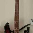 Elektrická basová kytara s trupem v barevném přechodu od žluté přes oranžovou k černé. Nástroj má hnědý hmatník, perleťový pickguard a chromované čás…